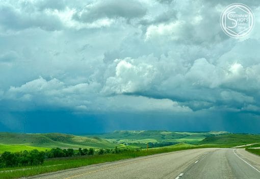 a road with green hills and clouds