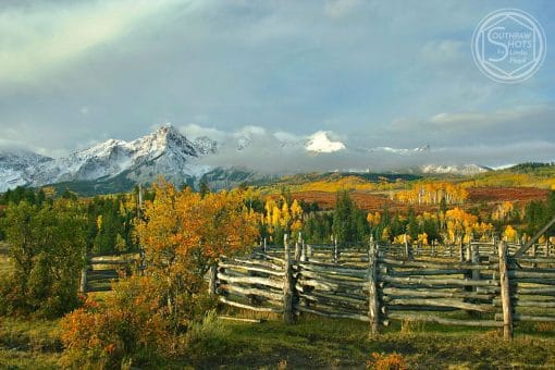 a fence in a field with trees and mountains in the background