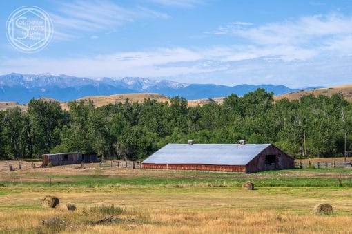 a barn in a field with trees and mountains in the background