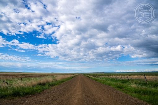 a dirt road with grass and blue sky